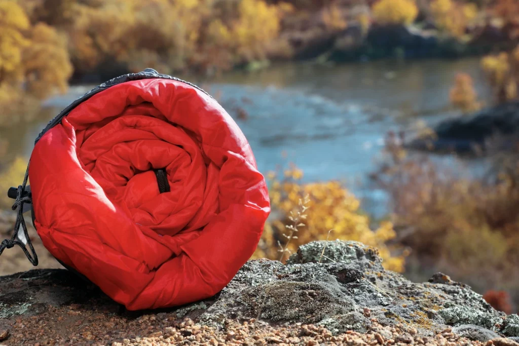 a photo of red rolled up sleeping bag on a rock overlooking a stream.