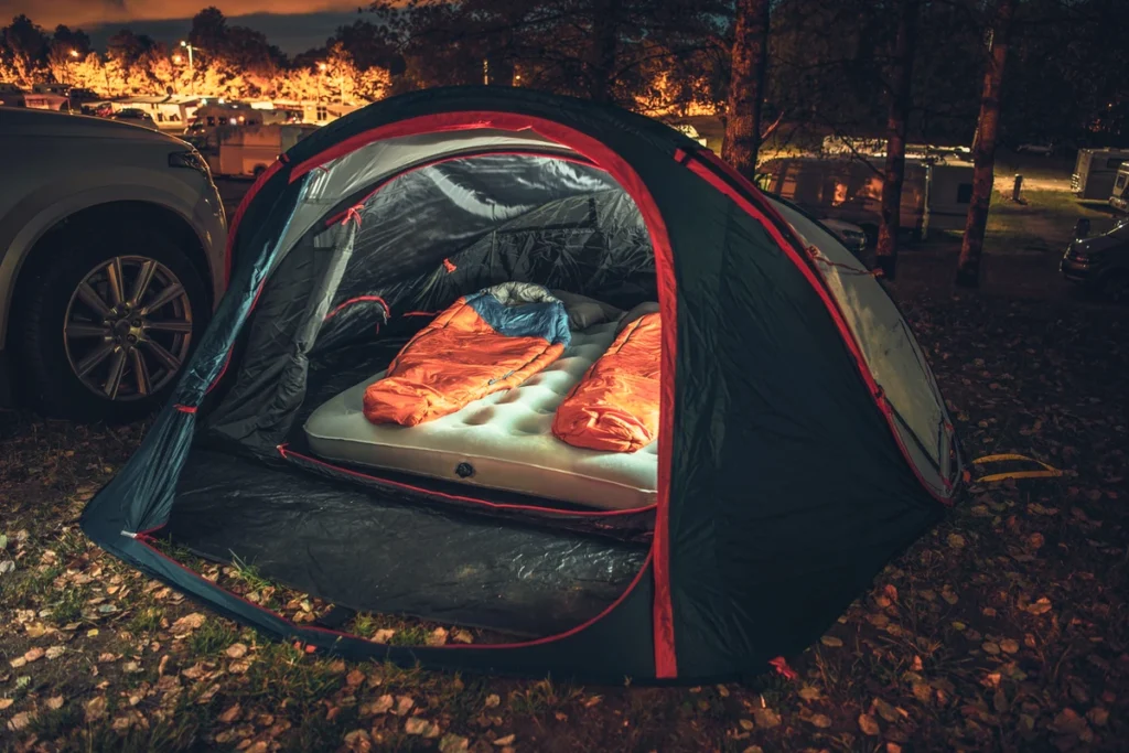 2 sleeping bags in a tent on a blow up mattress illuminated from inside the tent.