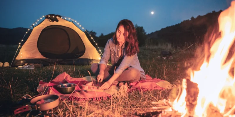 a photo of a woman camping alone at night with a camp fire