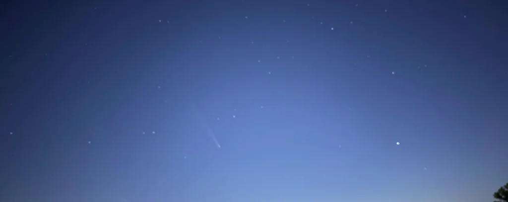 Comet Tsuchinshan-ATLAS with its faint tail against a deep blue twilight sky dotted with stars, shot on an iPhone on a magnetic tripod
