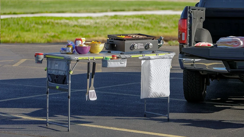 CORE FlexRail prep and cook table set up behind a pickup tailgate with a griddle, food, utensils and a hanging trash bag