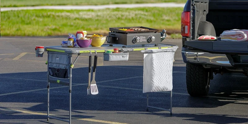 CORE FlexRail prep and cook table set up behind a pickup tailgate with a griddle, food, utensils and a hanging trash bag